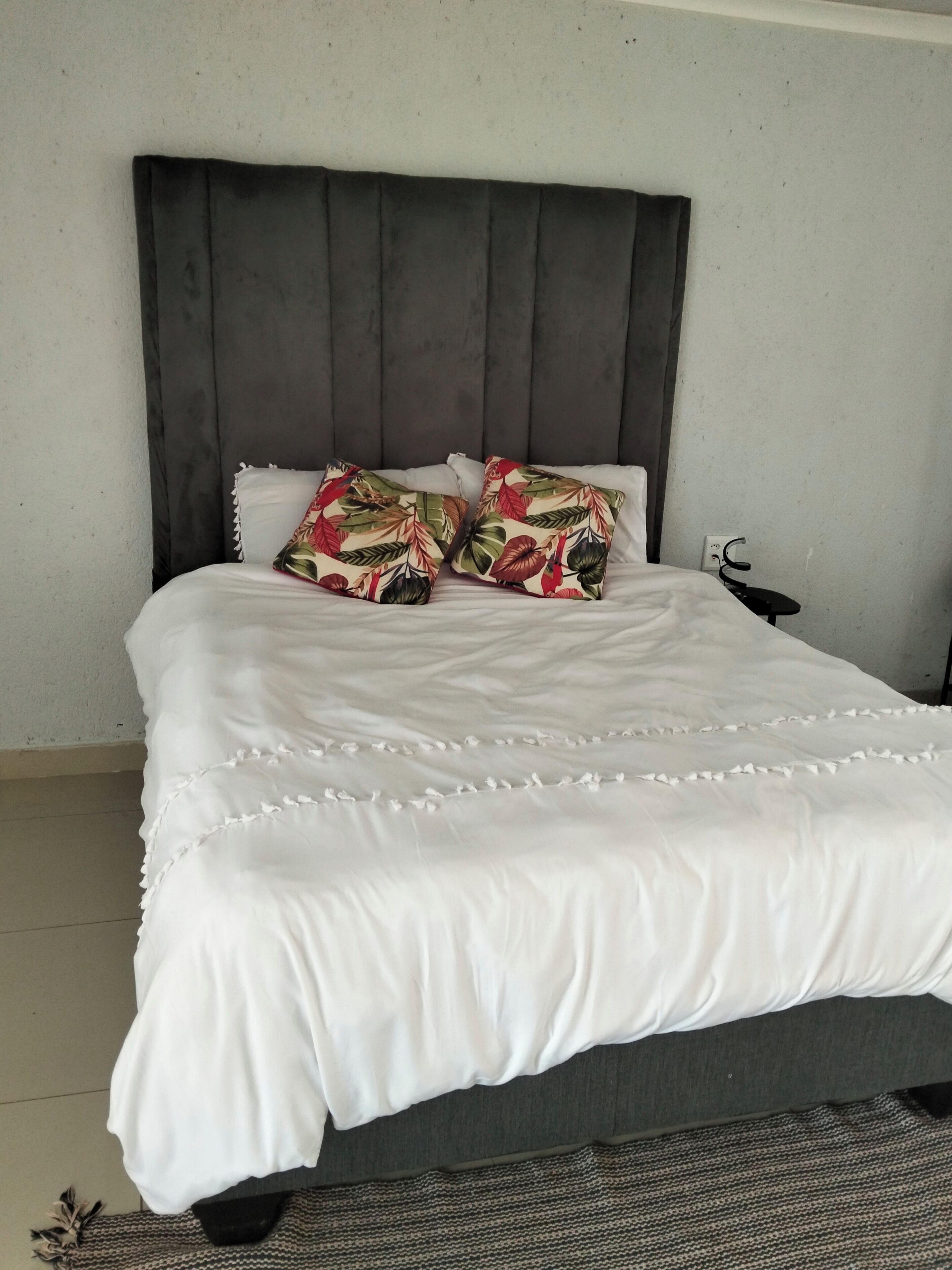 A bed with a dark headboard, white bedding, and two floral pillows.