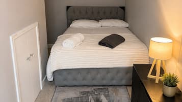 Quarto bem arrumado com cama, mesa de cabeceira, abajur e uma pequena planta em vaso.