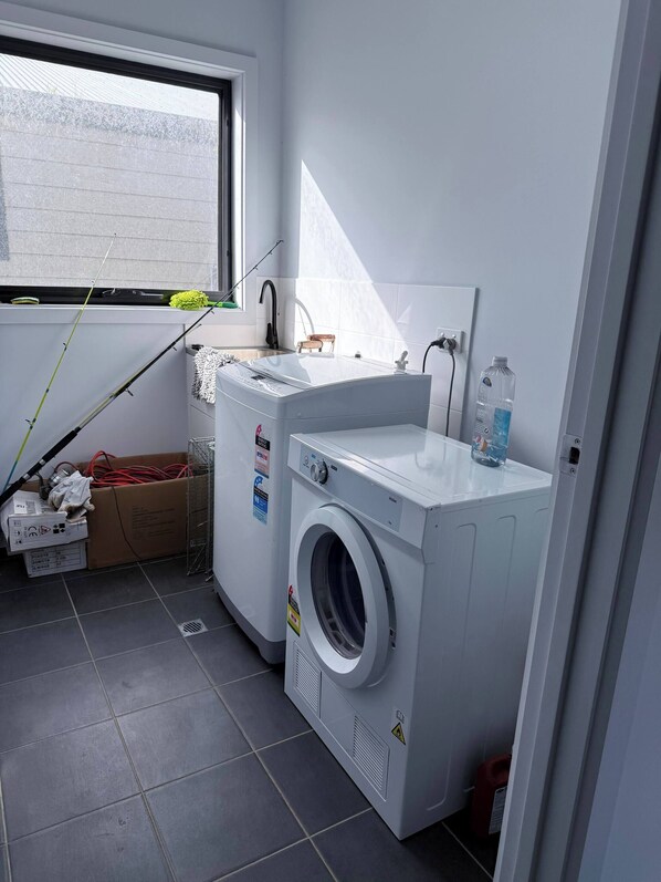 A laundry room with a washing machine, a sink, and a window.