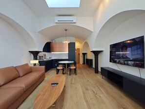 A modern living room with a sofa, a coffee table, a TV, and a kitchen area in the background. - free parking, Nuslesky Pivovar Blue Arch Luxury Apartment With Garden (Hlavní město Praha city)