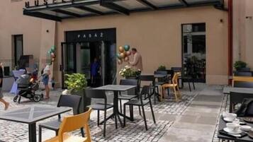 An outdoor seating area with tables and chairs, a covered entrance, and a building with signage.