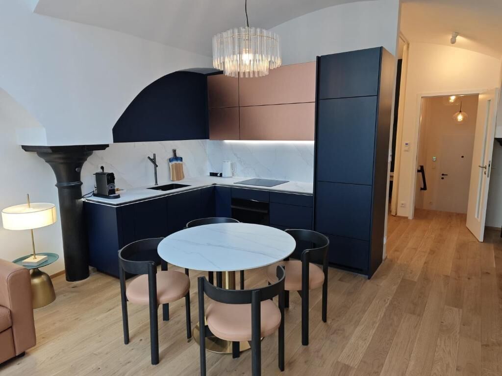 A modern kitchen with a dining area, featuring a round table and chairs, a built-in oven, and a pendant light.