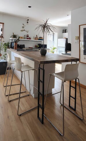 A modern kitchen with a central island, bar stools, and a potted plant. - Large urban apartment with steam sauna 1 (Montreal)