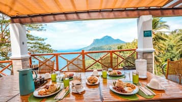 A dining table set outdoors with a view of a mountain and ocean.