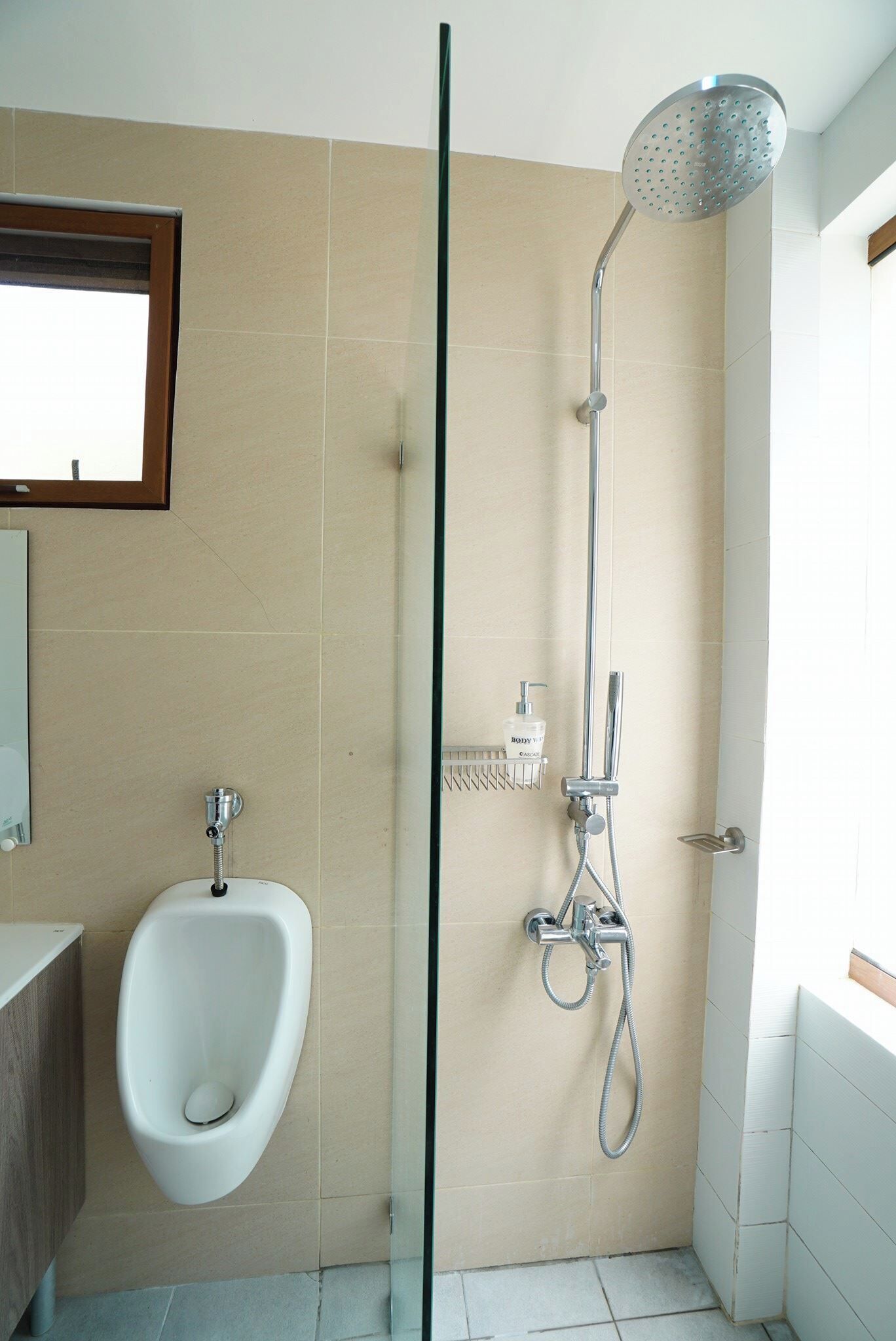 A modern bathroom with a urinal, a glass shower enclosure, and a handheld showerhead.