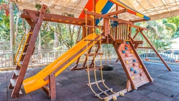 A playground with a slide, climbing net, and a tire swing.