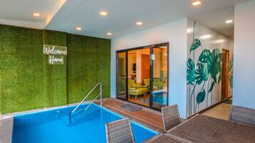 A swimming pool with a glass enclosure, a 'Welcome Home' sign, and a room with a green wall and tropical leaf mural.