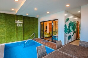 A swimming pool with a glass enclosure, a 'Welcome Home' sign, and a room with a green wall and tropical leaf mural.