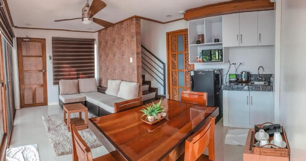 A modern living space with a wooden dining table, sofa, and kitchen area.