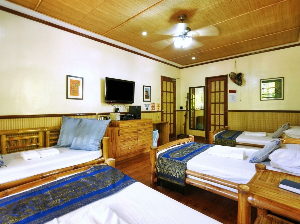 A hotel room with two beds, wooden furniture, a television, and a ceiling fan.