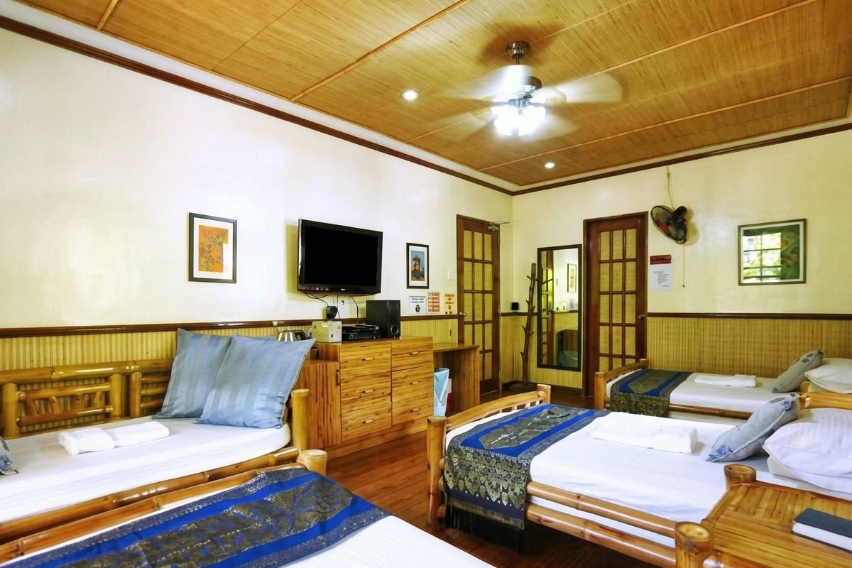 Habitación de hotel con dos camas, muebles de madera, televisor y ventilador de techo.