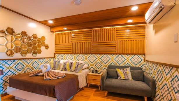 Una habitación de hotel con una cama, un sofá, una mesita de noche y una pared con diseños geométricos.