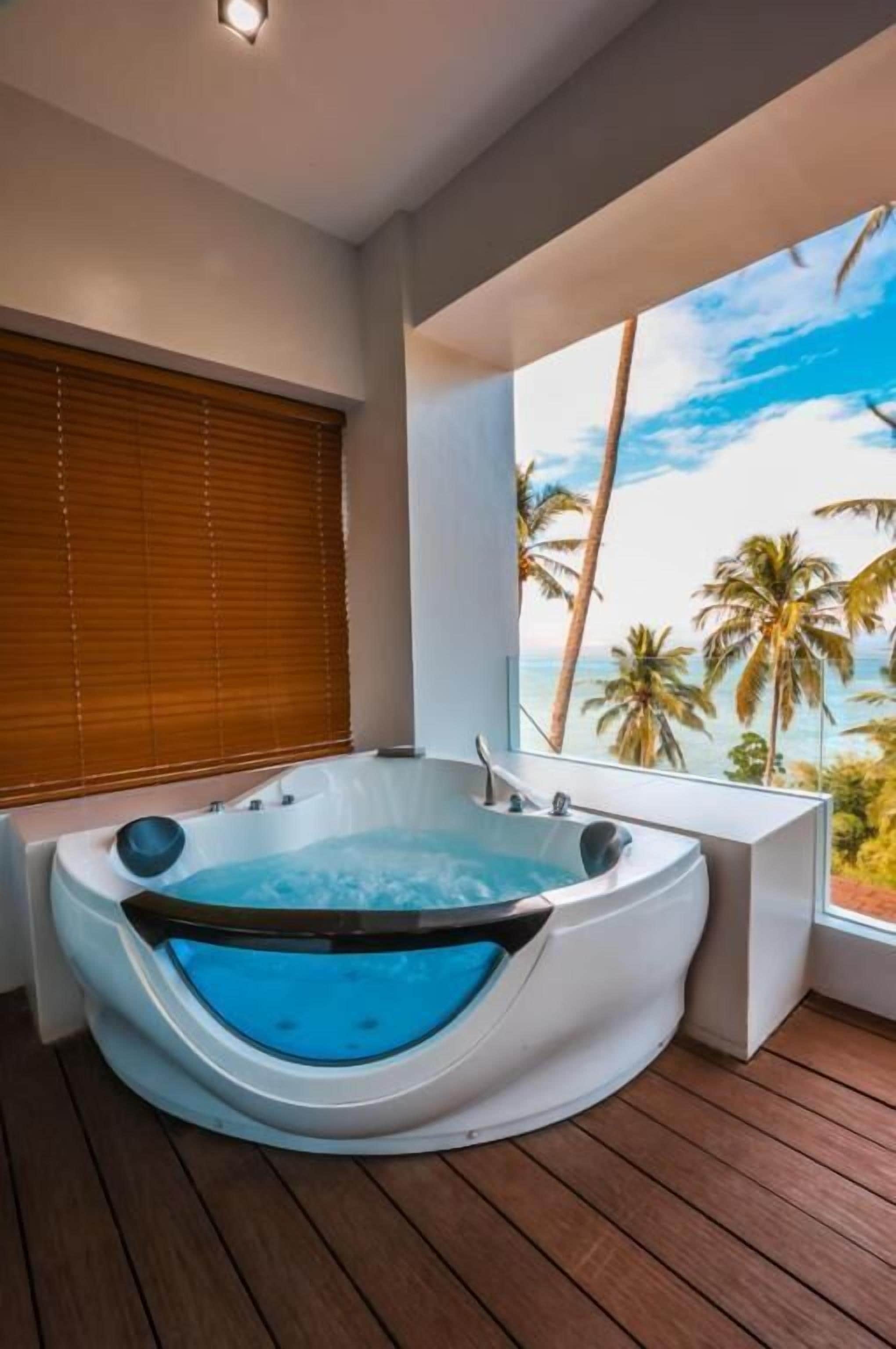 A hot tub on a wooden deck with a view of palm trees and the sky.