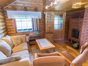 A cozy log cabin interior with a sofa, armchair, wooden table, and a fireplace.