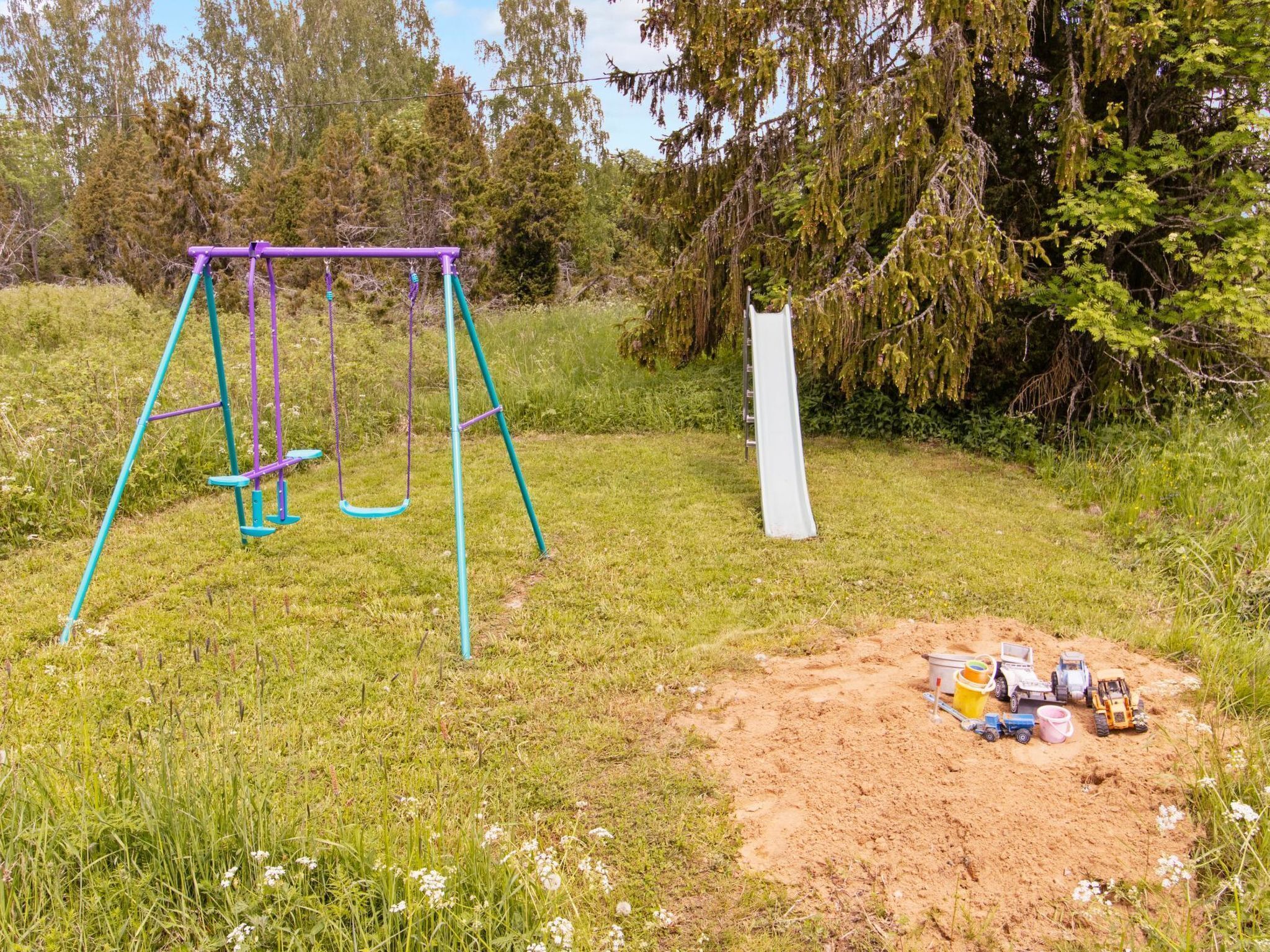 Ein Spielplatz mit Schaukeln und einer Rutsche, umgeben von Gras und Bäumen.