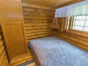 A small, wooden cabin room with a single bed, a window with a curtain, and a wooden wardrobe.