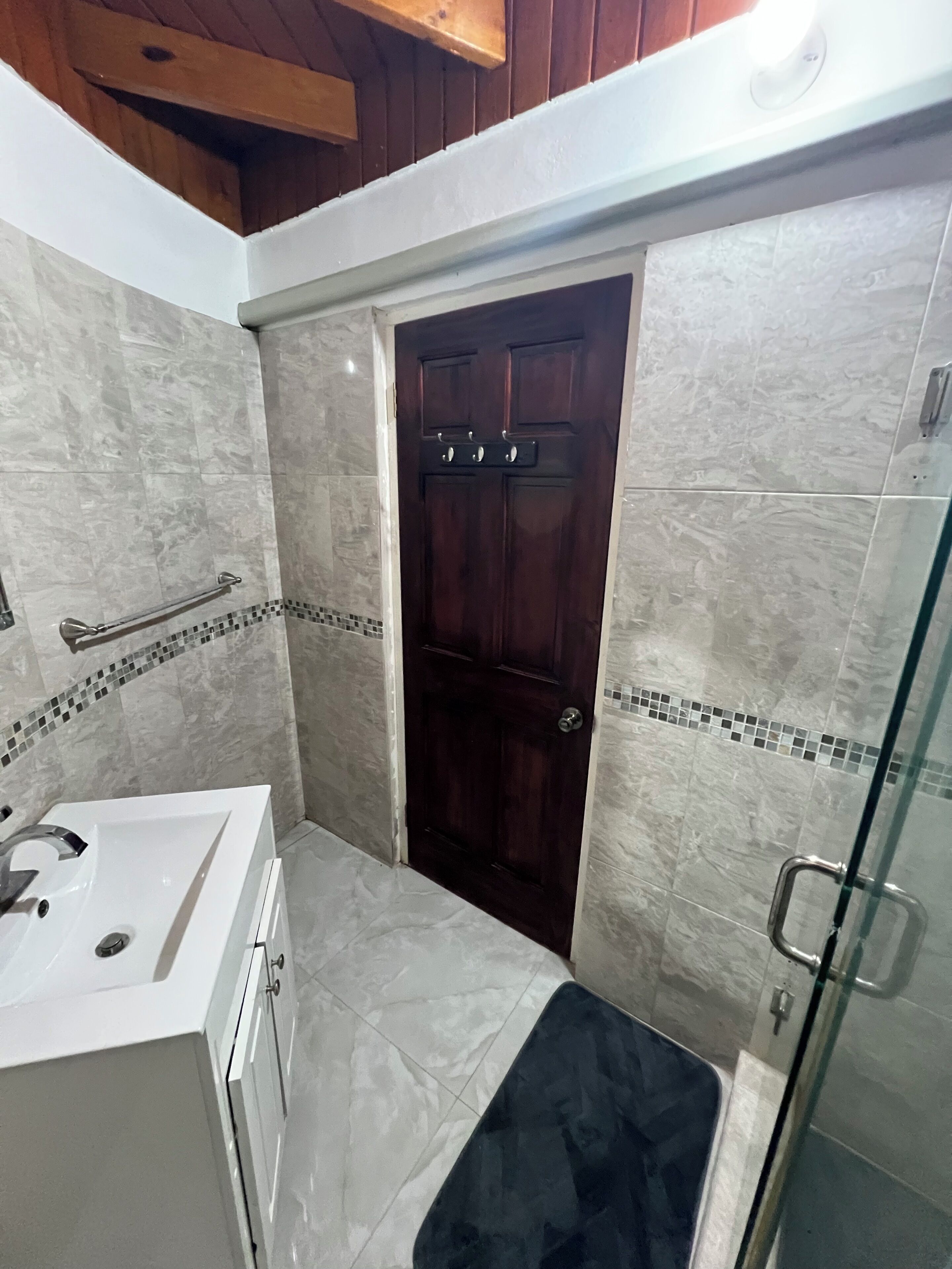 Un baño con un lavamanos blanco, una puerta de madera oscura y una cabina de ducha de vidrio.