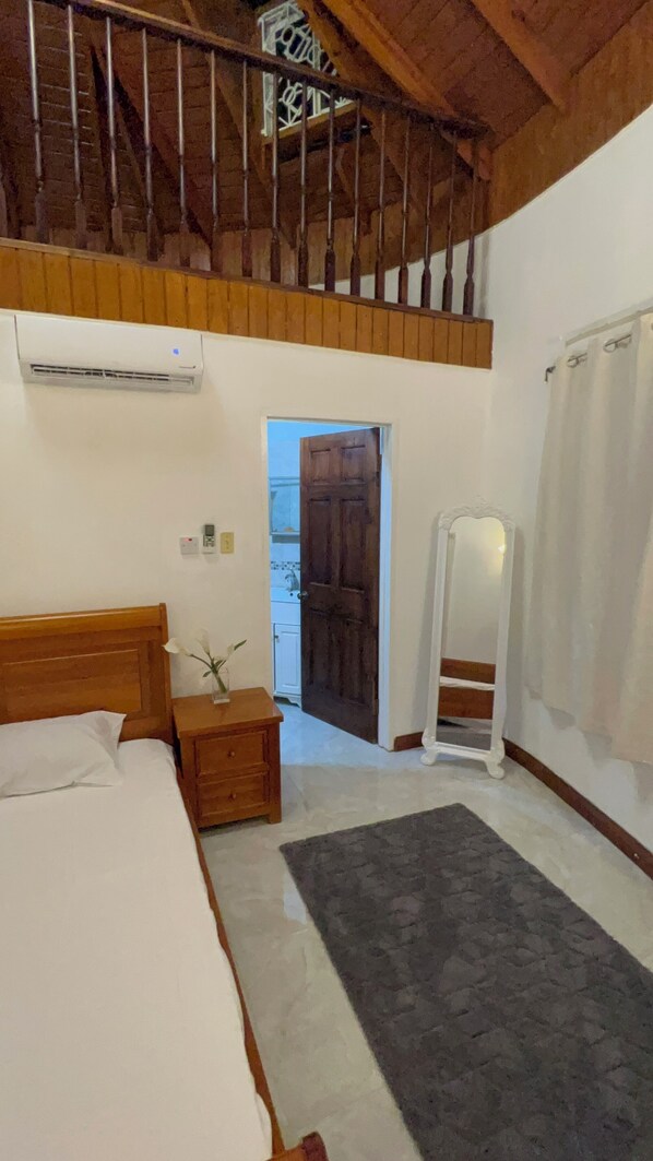 A bedroom with a bed, bedside table, nightstand, mirror, and a door leading to a bathroom.