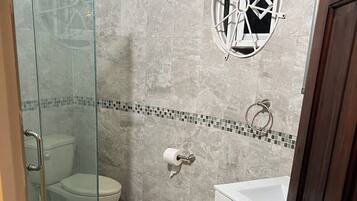 A bathroom with a glass shower enclosure, a toilet, a sink, and a decorative window.