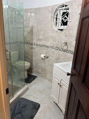 Een badkamer met een douchecabine van glas, een toilet, een wastafel en een decoratief raam.