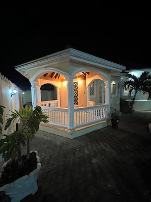 A small, white, two-story building with a balcony and a covered porch area.