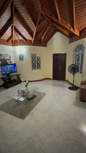 A room with a sloped ceiling, a television, a fan, and a door.