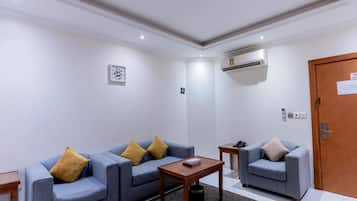 A room with a sofa set, a small table, a door, and an air conditioning unit.