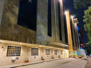 Un edificio con una serie de ventanas verticales y un área de acceso pavimentada.