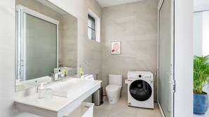 A modern bathroom with a large mirror, white sink, toilet, and a front-loading washing machine. - Buddha Bliss Luxury Villa (Tambon Ko Pha-Ngan)