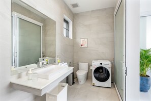 A modern bathroom with a large mirror, white sink, toilet, and a front-loading washing machine. - Buddha Bliss Luxury Villa (Tambon Ko Pha-Ngan)