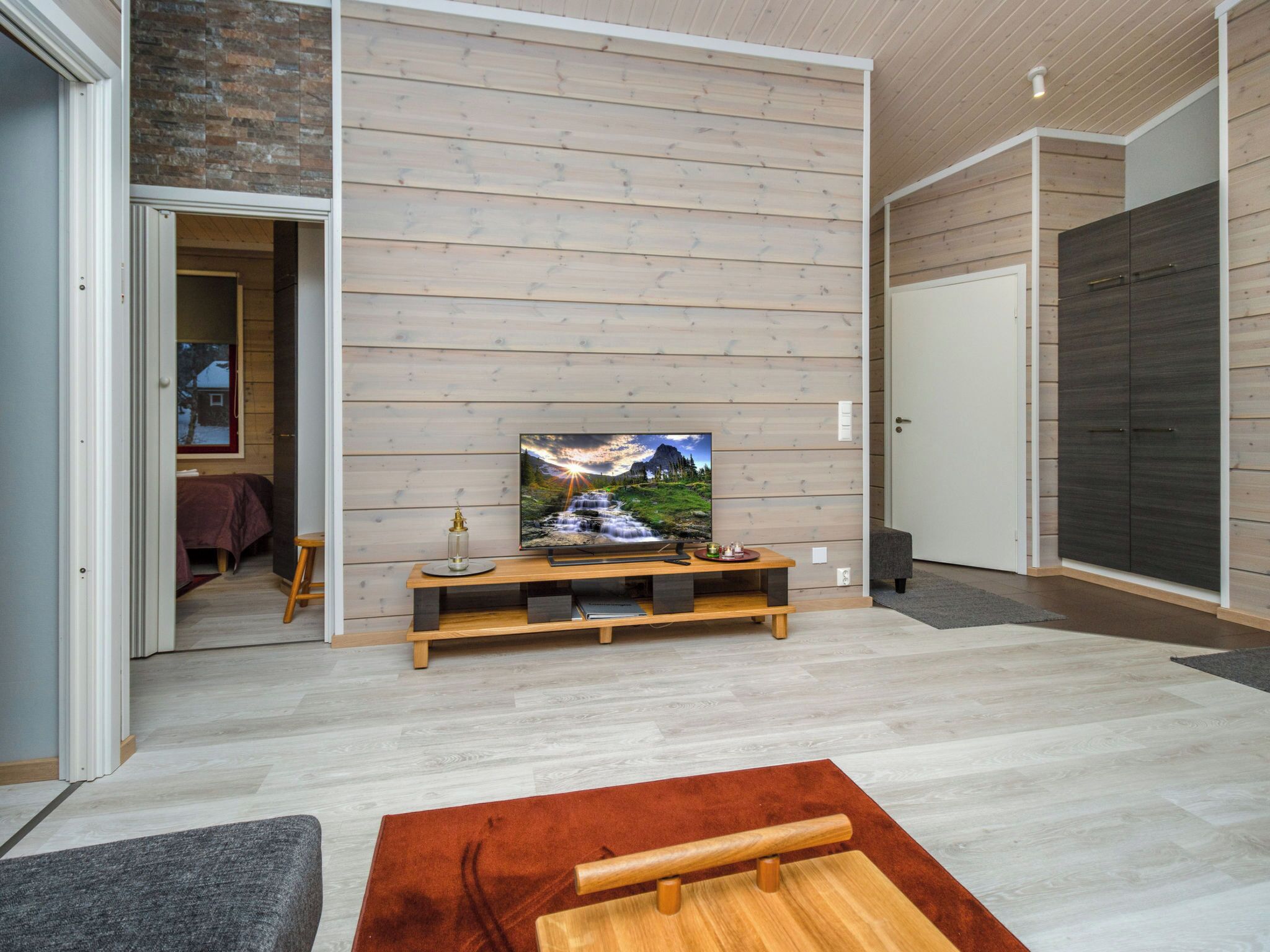 A modern living room with a television on a wooden stand, a red rug, and a grey sofa.