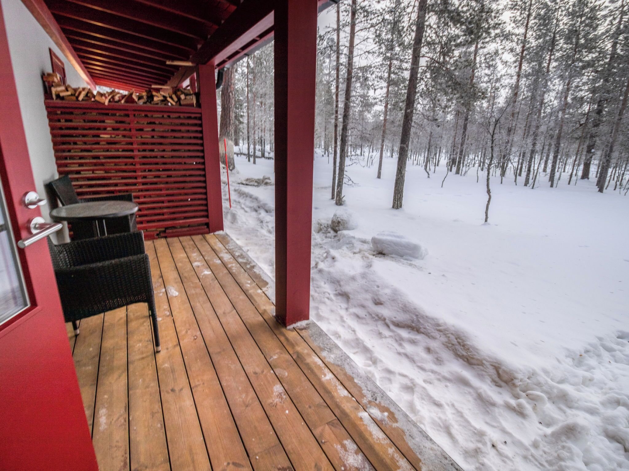 Eine Holzterrasse mit überdachter Sitzecke und Kamin, vor verschneiter Waldlandschaft.