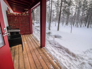 A wooden deck with a covered seating area, a fireplace, and a snowy forest backdrop. - Tuiskukuru b by Interhome (Inari)