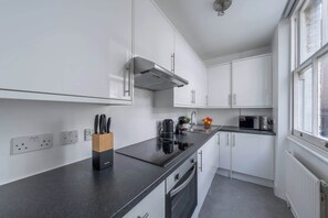 A modern kitchen with white cabinets, a black countertop, a built-in stove, and a window providing natural light. - Bright Central 1BR 1BA steps from Oxford Street (London)