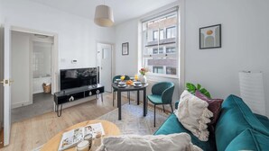 Een moderne woonkamer met een televisie, eettafel en een blauwgroene bank.