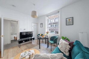 A modern living room with a TV, dining table, and teal sofa. - Bright Central 1BR 1BA steps from Oxford Street (London)