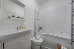 A modern bathroom with a white sink, toilet, and bathtub. There are shelves with toiletries and a small plant. - Bright Central 1BR 1BA steps from Oxford Street (London)
