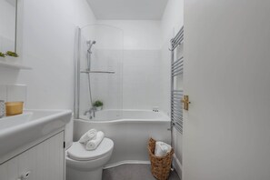 A compact bathroom with a toilet, a bathtub, and a shower. - Bright Central 1BR 1BA steps from Oxford Street (London)