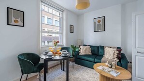 Een moderne woonkamer met een blauwgroene bank, een eettafel met ontbijtartikelen en kunstwerken aan de muur.