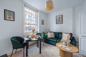 A modern living room with a teal sofa, a dining table with breakfast items, and artwork on the walls. - Bright Central 1BR 1BA steps from Oxford Street (London)
