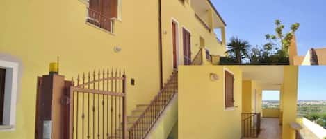 Edificio amarillo con entrada porticada, una escalera y un balcón con vistas al paisaje.