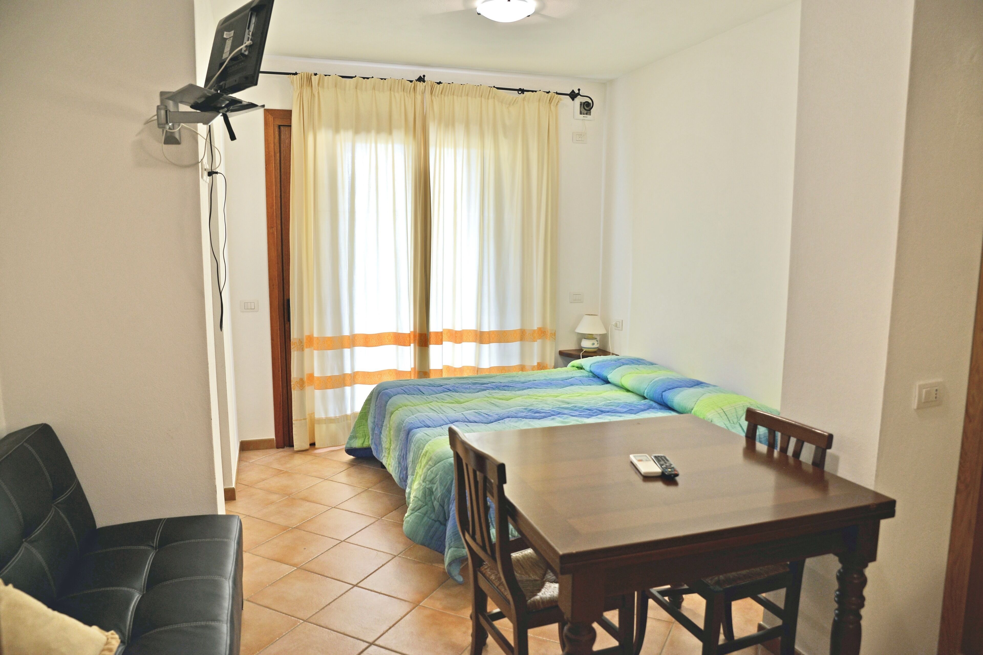 Um quarto com uma cama, uma mesa, uma cadeira e uma televisão.