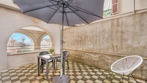 En udendørs patio med skakternet gulv, et bord, stole og en stor parasol.