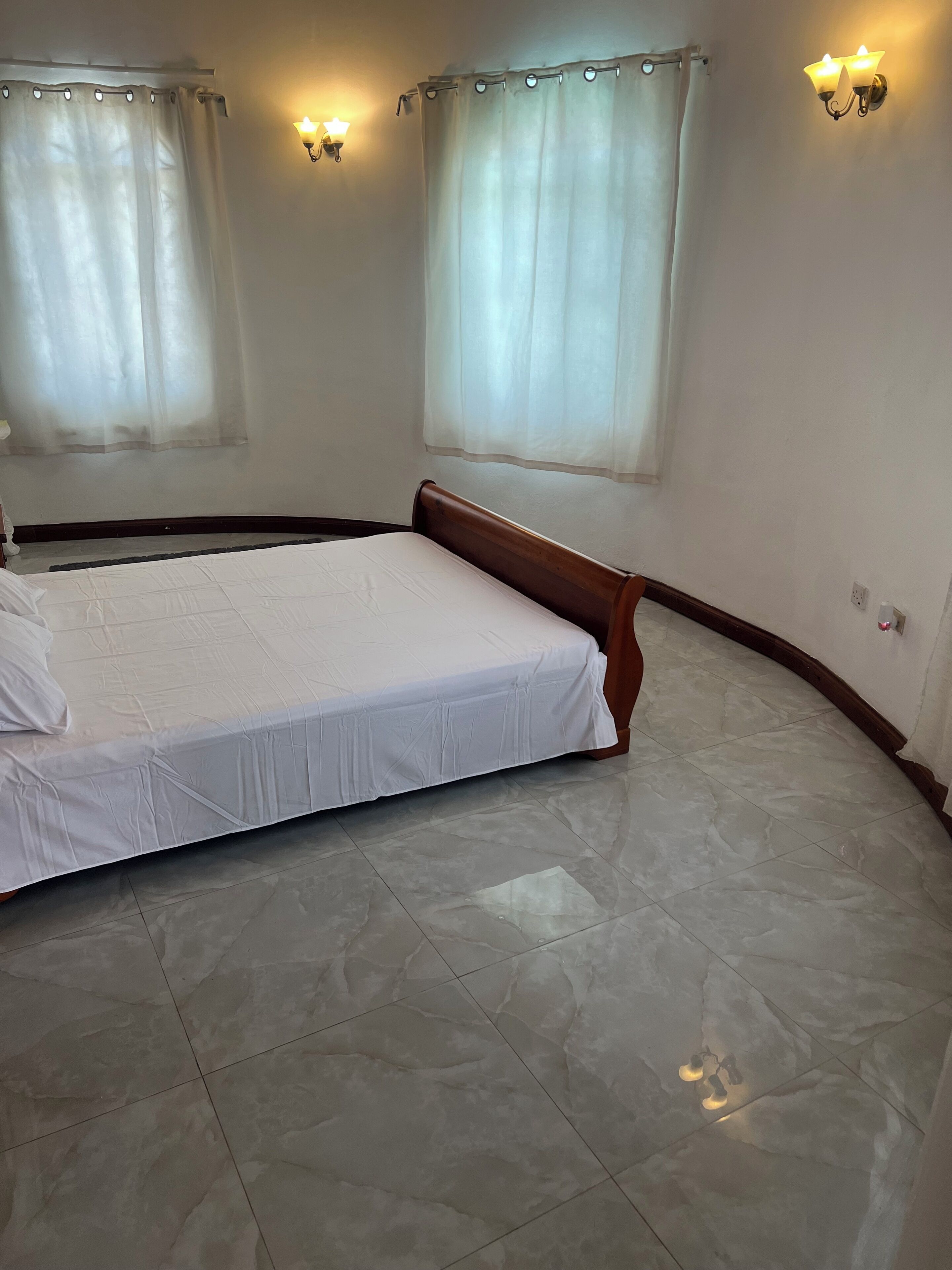 A bedroom with a bed, two wall-mounted light fixtures, and a window with a curtain.