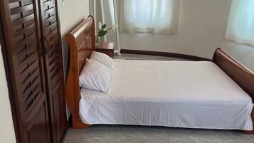 Ein Schlafzimmer mit einem Einzelbett, einem Holzschrank, einem Spiegel und einem Fenster mit Vorhang.