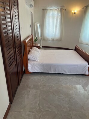 A bedroom with a single bed, a wooden wardrobe, a mirror, and a window with a curtain.