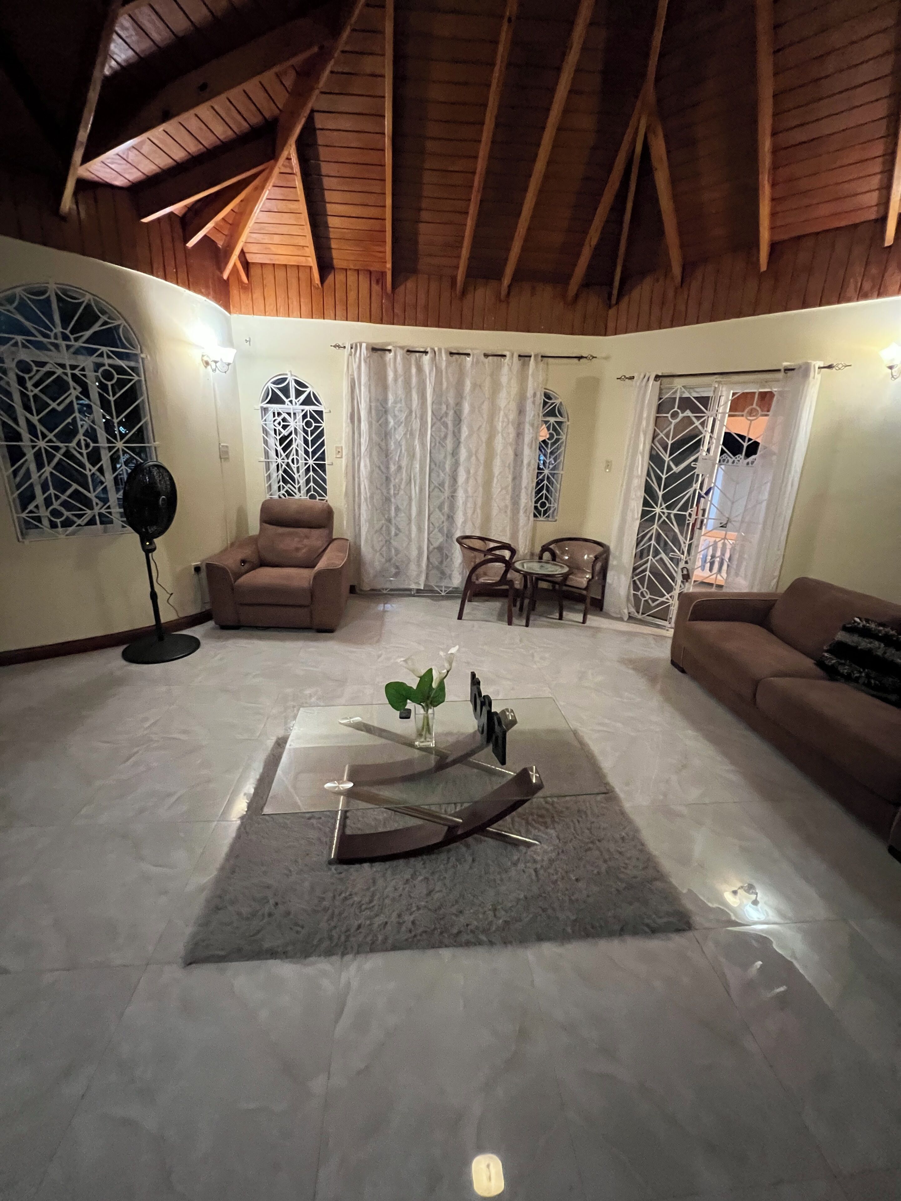 A living room with a sofa, armchairs, a coffee table, and a fan.