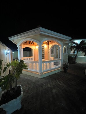 A small, white, two-story building with a balcony and a covered porch area.