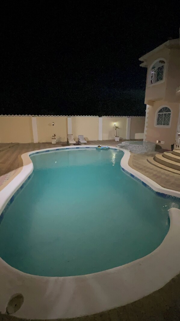 A swimming pool with a curved edge, surrounded by a low wall and a few chairs.