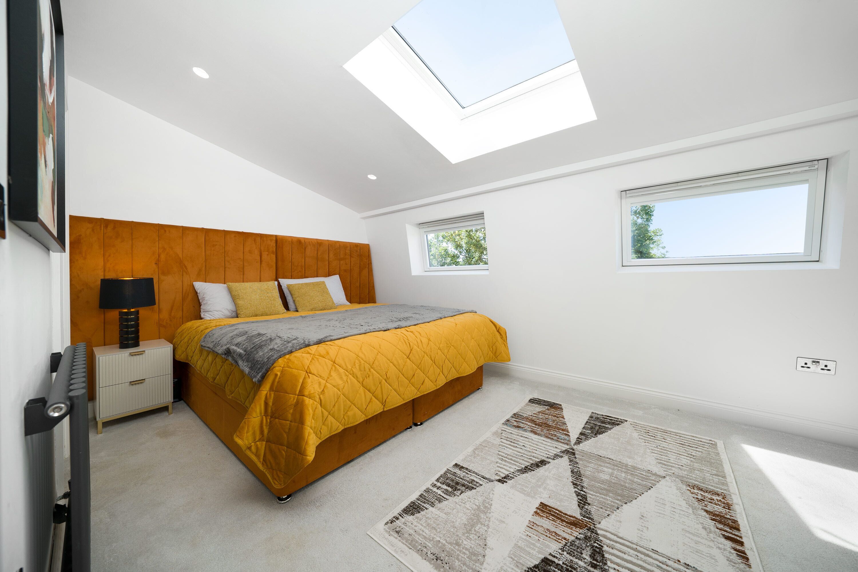 A bedroom with a bed, bedside table, lamp, and a skylight.